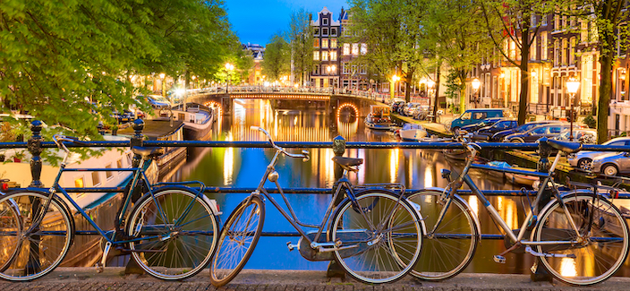 Old bicycles on the bridge in Amsterdam, Netherlands against a canal during summer twilight sunset. Amsterdam postcard iconic view. Tourism concept.